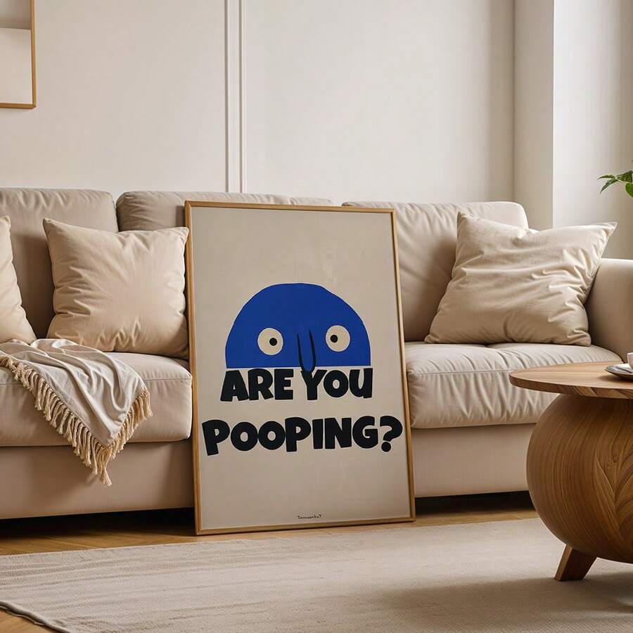 Framed ARE YOU POOPING funny blue face print leaning against cream sofa in neutral living room