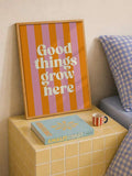 Framed orange and pink Good things grow here art on a yellow tiled bedside table