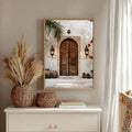 Natural wood framed arched door canvas above a white dresser with lanterns pottery palm leaves pink blooms and red accents
