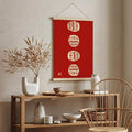 Red canvas poster with four cream Daruma dolls arranged vertically