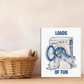 Navy cat climbs from an open washing machine on white canvas beside a wicker laundry basket