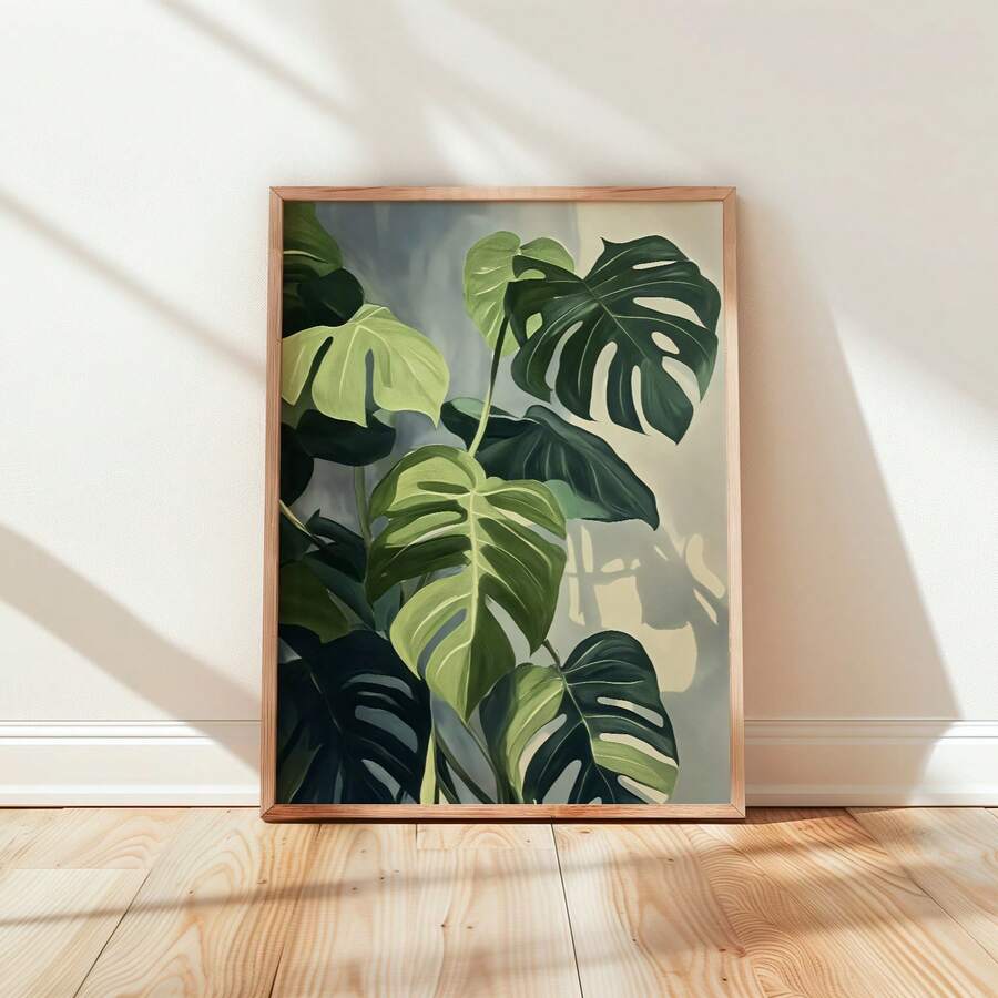 Framed monstera botanical wall art leaning against cream wall on pale wood floor in diagonal sunlight