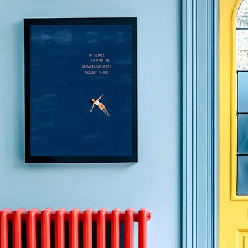 Vertical navy quote print with floating woman in black frame on a blue wall