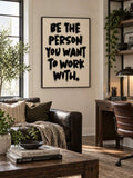 Framed cream canvas with bold black brush lettering above a leather sofa