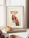 Pale-framed jeweled hand artwork with pink coupe drink beside a bright window