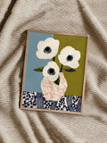 Three white anemones in a blush vase against blue and olive panels with navy floral border