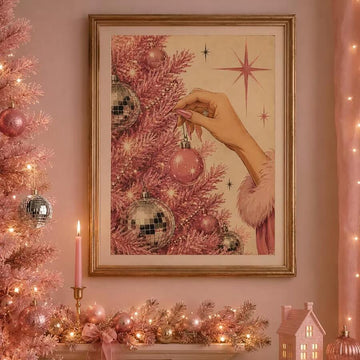 Gold-framed pink Christmas tree print with a hand hanging a bauble above a festive mantel