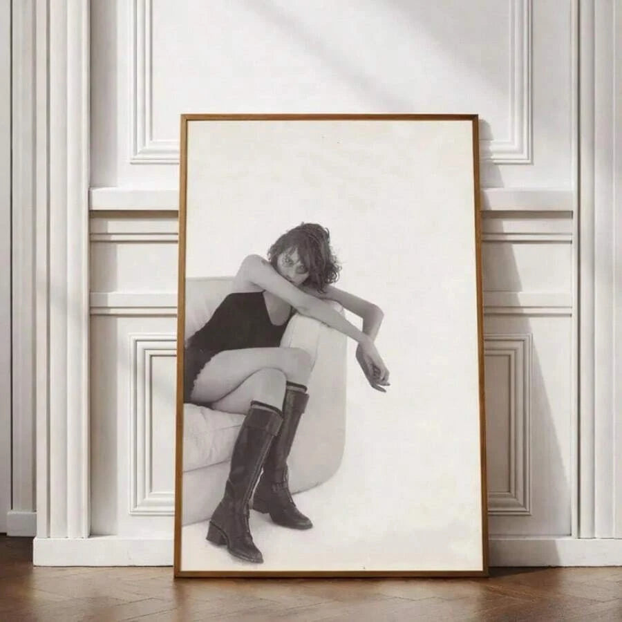Black-and-white fashion portrait of a woman in knee-high boots seated in an armchair, framed against a white paneled wall
