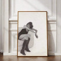 Black-and-white fashion portrait of a woman in knee-high boots seated in an armchair, framed against a white paneled wall
