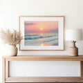 front framed view of Framed coastal wall art print showing ocean waves, beach shoreline, sunrise or sunset sun, pastel sky and soft modern beach house colors.