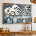 White daisies in blue glass jars with blue butterflies and an encouraging quote in a wood-toned frame above a rattan-front sideboard