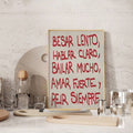 Red Spanish quote print leaning against a kitchen wall beside glassware and wooden serving boards