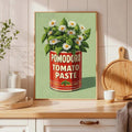 Framed tomato paste can and daisy print leaning on a kitchen counter