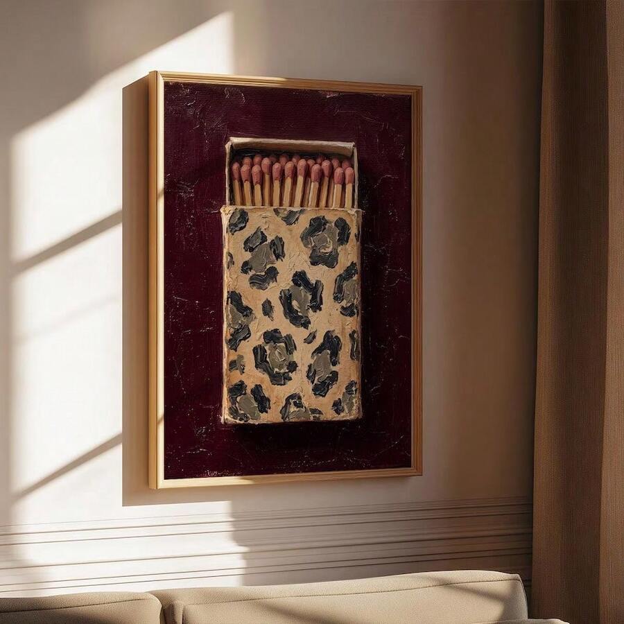 Framed burgundy matchbox canvas poster with leopard-print artwork displayed above a console in warm sunlight
