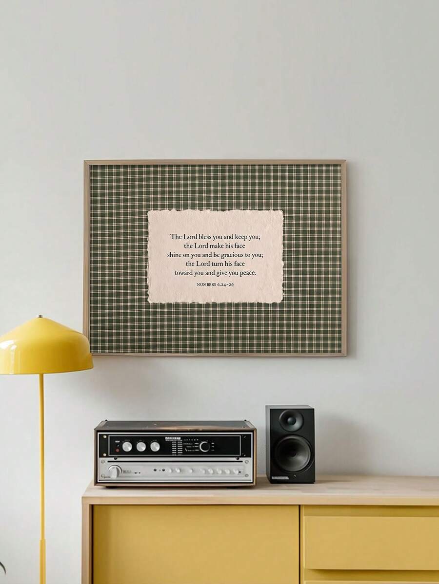 Green gingham blessing artwork in a light wood-toned frame above a stereo and yellow cabinet beside a yellow lamp