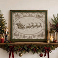 Antique-style Santa sleigh and four reindeer canvas artwork in a dark green and gold-toned frame on a Christmas mantel with garland and candles