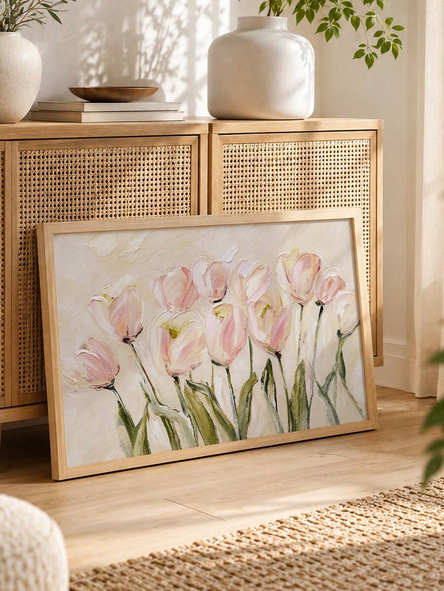 Wide framed canvas of loose pink tulips with green stems on a cream ground leaning by a rattan cabinet